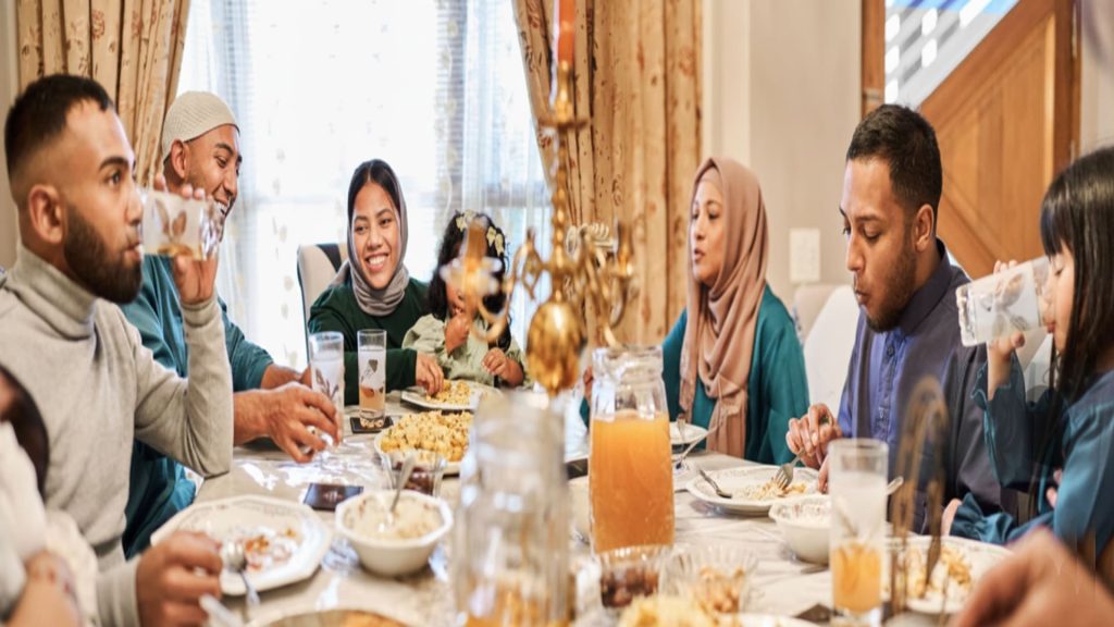 A Muslim family sits around the dining table eating Eid food during Ramadan Iftar time.