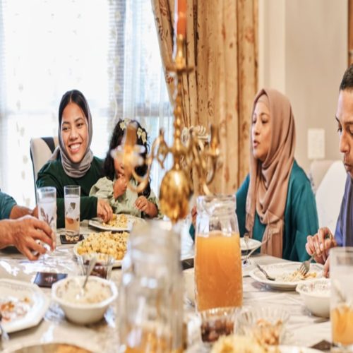 A Muslim family sits around the dining table eating Eid food during Ramadan Iftar time.